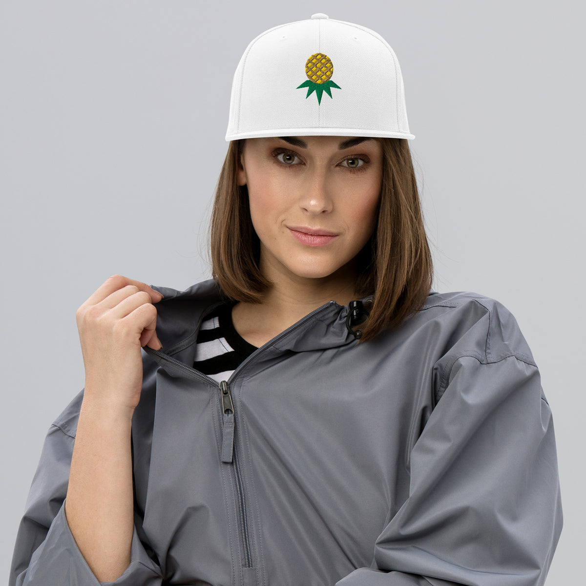 White flat-brim snapback with embroidered upside-down pineapple, front view on model
